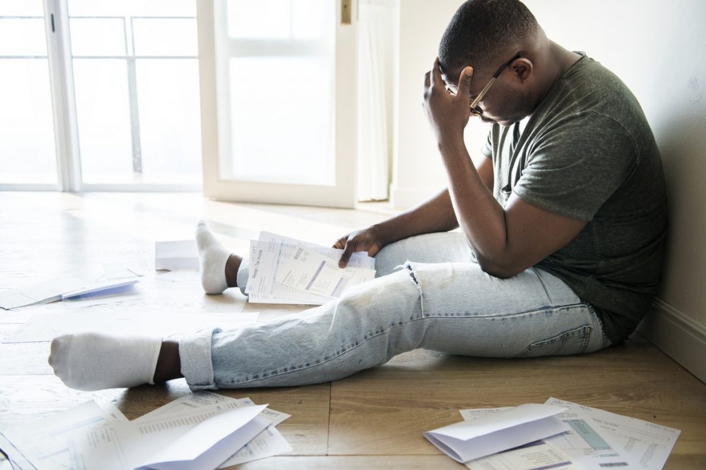 Man sitting on floor looking at bills.